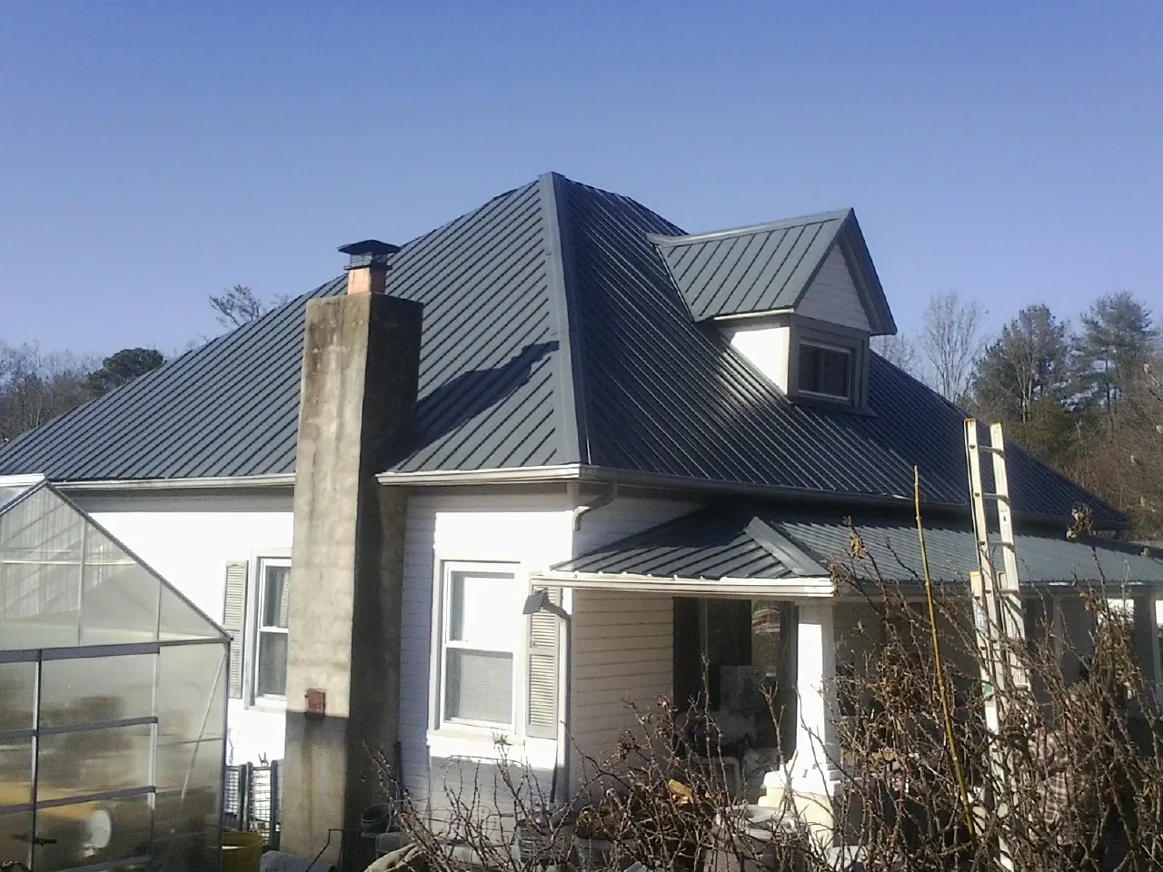 Dark blue standing seam metal roof on a white farmhouse with dormer — Slate & Tile Roof Repair by Roofing Brothers in Mountainville