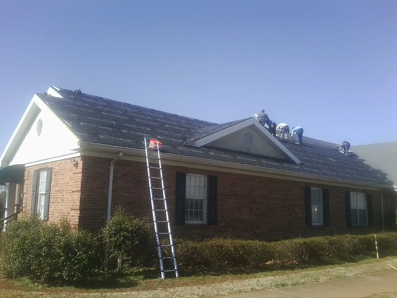 Crew tearing shingles off a brick ranch roof with a ladder set — Emergency Roof Repair work by our crew in Mountainville