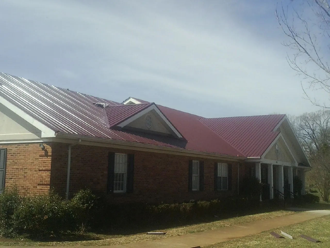 Red metal roof with gabled entries on a long brick building, from a Hail Damage Roof Repair job in Mountainville