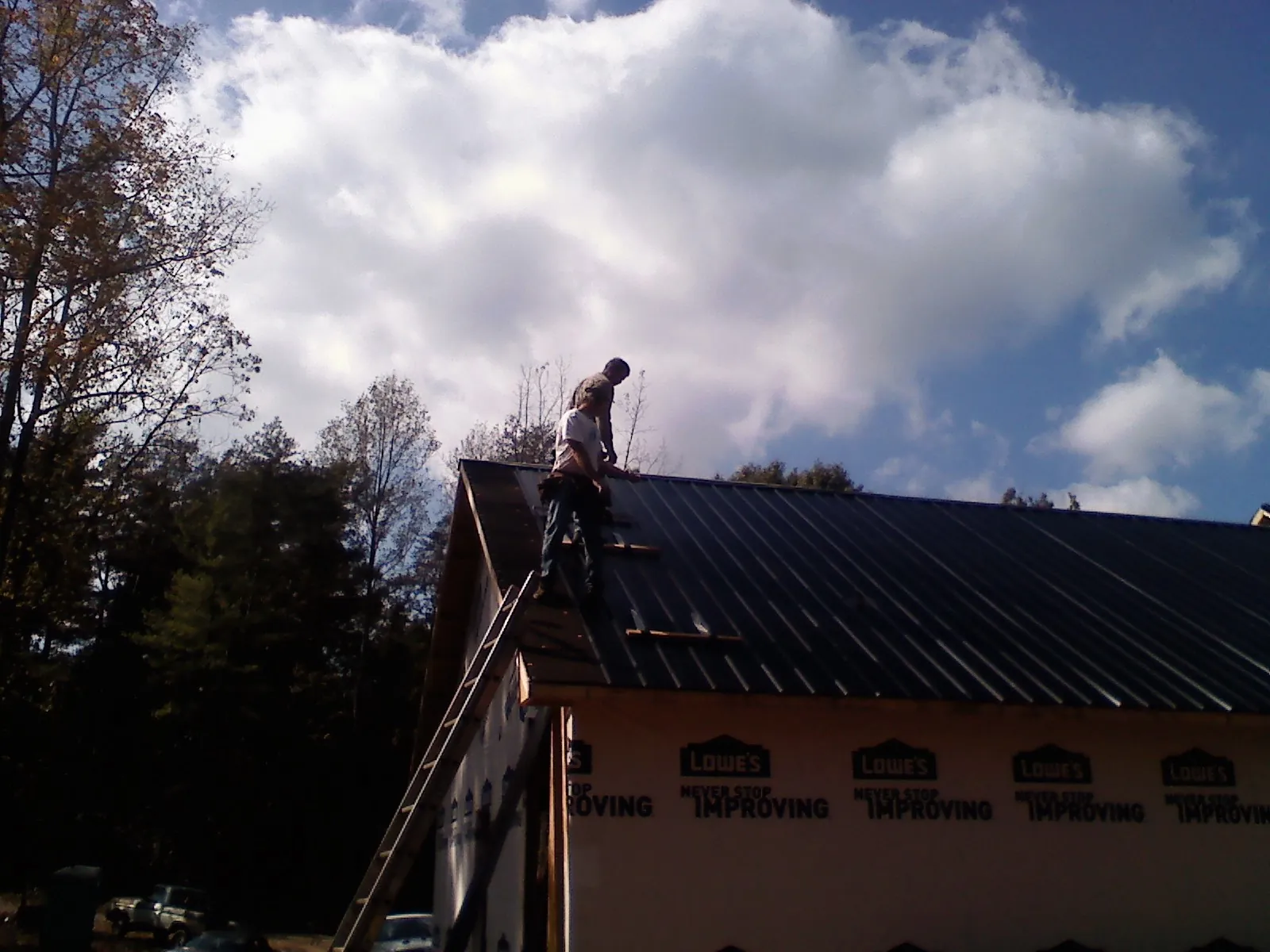 Roofer fastening dark metal panels high against a cloudy sky, from a Roof Inspection job in Mountainville