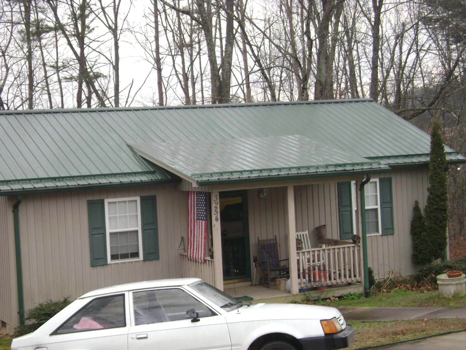 Green metal roof and front porch on a tan sided cottage in Mountainville