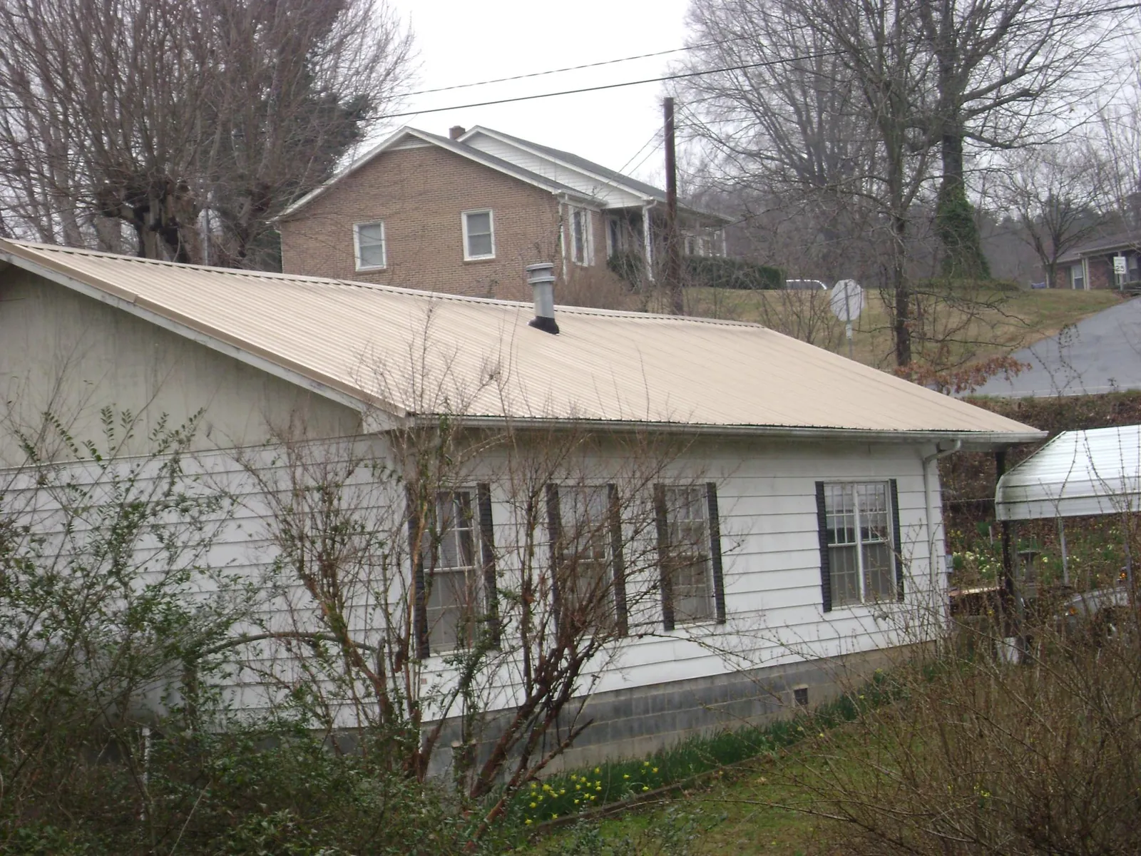 Tan metal roof on a white sided house set into a hillside — Commercial Roofing by Roofing Brothers in Mountainville